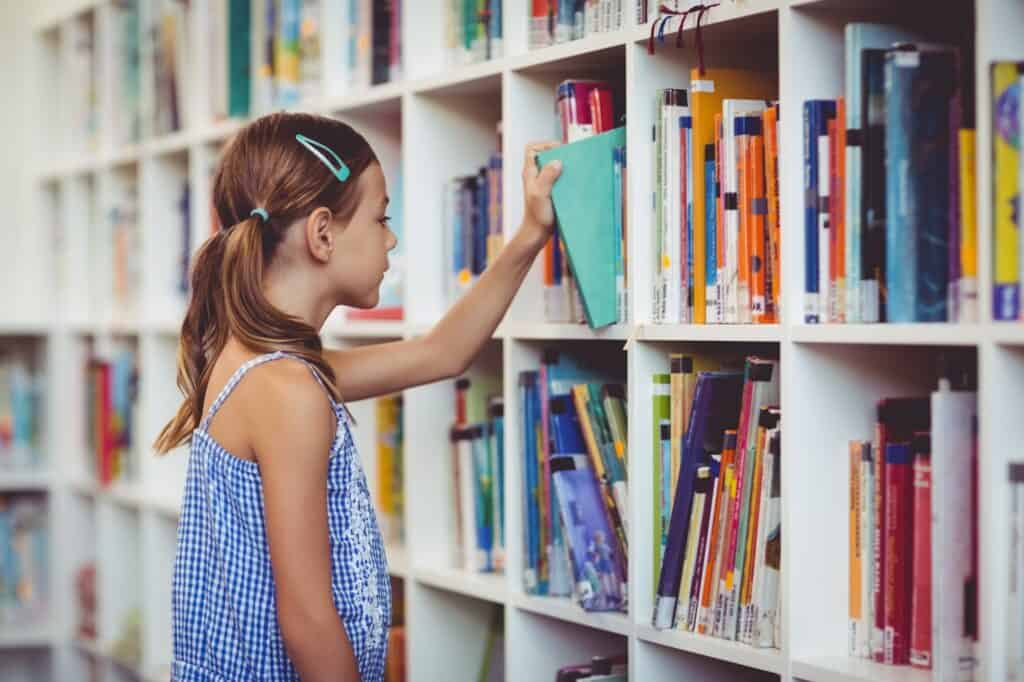 A school girl taking a book from a bookshelf in the library in the concept of 'top schools in Romford'.