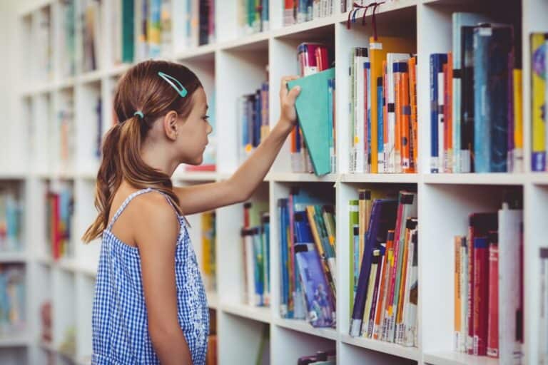 A school girl taking a book from a bookshelf in the library in the concept of 'top schools in Romford'.