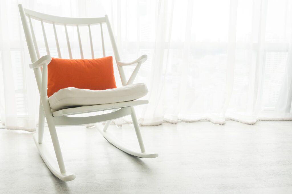 A white rocking chair with an orange pillow